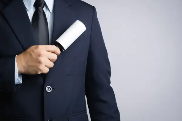 A man in a dark tuxedo uses a lint roller to clean his jacket, showing a simple way how to clean a tuxedo.