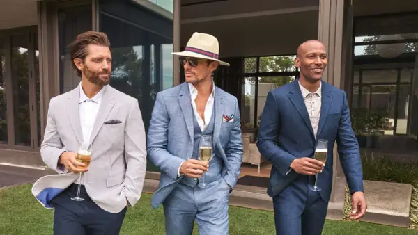 Stylish men in suits and blazers, perfect for ideas on what to wear to a wedding men. They hold champagne glasses.