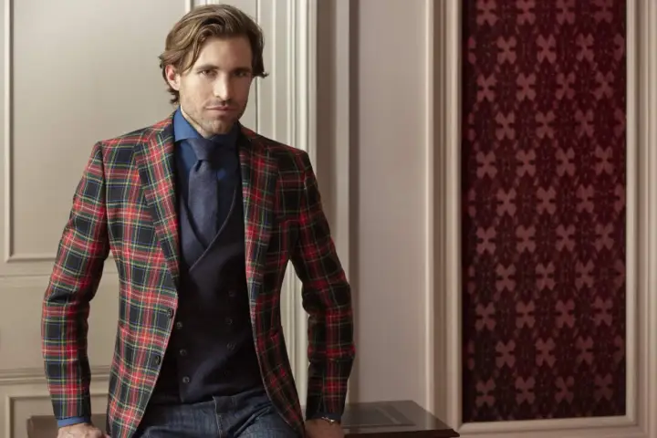 Man in a festive tartan blazer, dark blue shirt, tie, and vest. This is what holiday attire looks like.